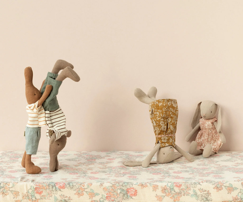 Four Maileg Bunny, Size 1 - Classic Flower Dresses, crafted from soft natural fabrics and recycled polyester, are playfully posed against a plain background. Two of them are performing a handstand, supported by each other. One Maileg Bunny, Size 1 - Classic Flower Dress is doing a headstand independently in floral bottoms while another sits cross-legged in a patterned dress.