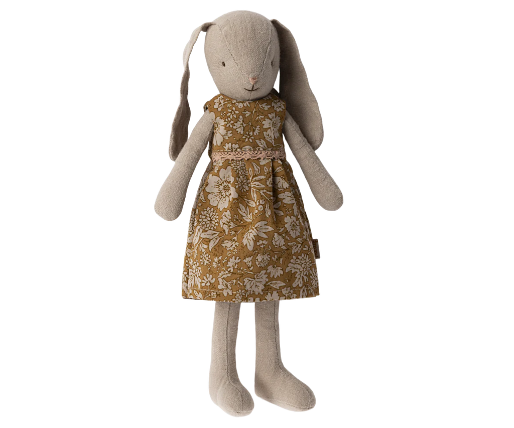 A Maileg Bunny, Size 2 - Flower Dress is dressed in a floral-patterned brown dress, crafted from soft natural fabrics. The bunny has long ears that hang down and a simple embroidered face. The dress features white flowers and leaves, giving it a vintage look. Made with recycled polyester, the toy stands upright with arms and legs extended.