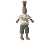 A Maileg Rabbit Size 2, Brown - Striped Blouse and Pants, crafted from soft natural fabrics and recycled polyester, dons a striped short-sleeve shirt and grey shorts. Standing upright with its arms and legs slightly apart, the Maileg Rabbit Size 2, Brown - Striped Blouse and Pants features long ears and a stitched facial expression.