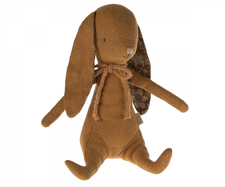 A soft bunny with long floppy ears, one of which has floral fabric on the inner side. The Maileg Bunny - Ocher, made from recycled polyester, features a small stitched nose and eyes, with a burlap ribbon tied in a bow around its neck. It has outstretched arms and legs.