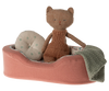 A small, stuffed toy cat wearing a knitted brown romper sits in the Maileg Small Cozy Bed - Coral. The bed features a cotton linen mattress and pillow, adorned with a beige polka dot cushion and a grey knitted blanket.