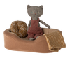 A handmade fabric cat doll wearing a red knitted overall sits in a Maileg Cozy Bed. The small pet basket includes a round, floral-patterned cushion and a soft blanket with yellow and white stripes draped over the side.