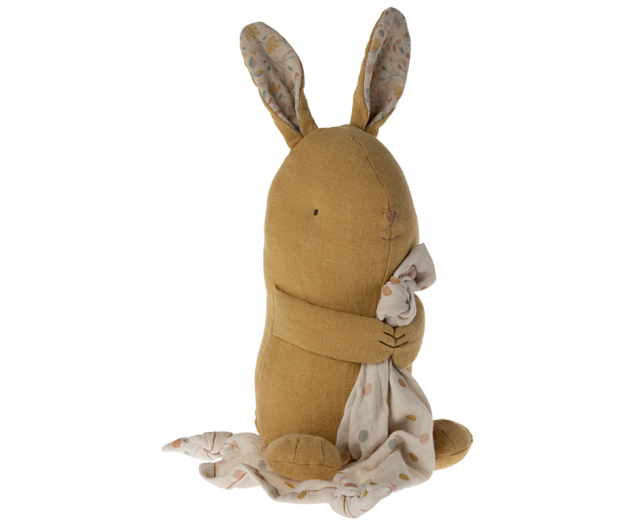 A Maileg Lullaby Friends - Bunny - Dusty Yellow (Plays Music) sits upright while holding a white blanket adorned with a colorful polka dot pattern. Part of the Lullaby Friends collection, this minimalist rabbit has an embroidered facial expression and its ears are lined with floral fabric, perfect for naptime with Mozart's lullaby.