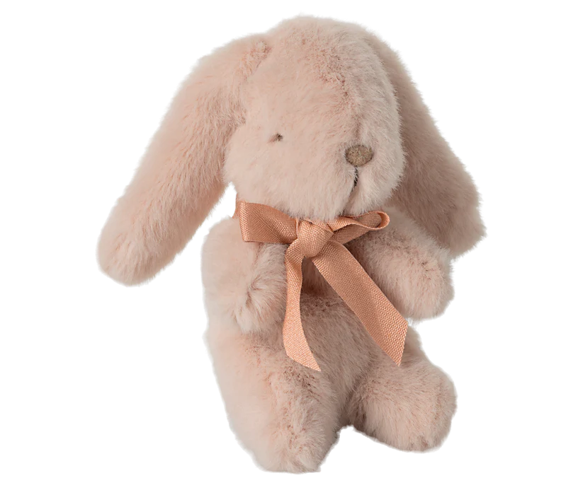 The Maileg Mini Plush Bunny - Powder is made from soft fabric and features a gentle pink hue with long, floppy ears. It boasts simple stitched eyes and nose that exude charm, while a peach satin ribbon bow elegantly adorns its neck.