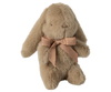 The Maileg Mini Plush Bunny in Dusty Brown is sitting upright, featuring long, floppy ears reminiscent of a plush bunny. Crafted from unique plush fabric, it is filled with polyester fillings for a soft and fluffy texture and adorned with a light brown ribbon tied in a bow around its neck.