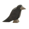 The Ostheimer Raven is a handcrafted wooden bird figurine, painted black with a contrasting gray beak and a lighter patch near the eye. It stands upright with its head slightly tilted forward, making it perfect for inspiring imaginative play as part of the Ostheimer toys collection.