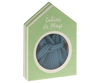 A green house-shaped gift box with a circular window displaying a folded blue Maileg Extra Clothing: Bathrobe - Dusty Blue inside. The box has white text at the top that reads "Cabine de Plage.