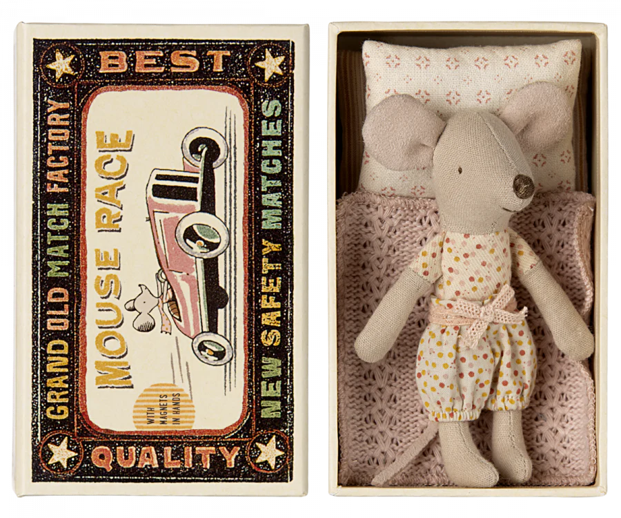 A small gray mouse toy, part of the Maileg Bathroom Starter Set, is nestled in a matchbox bed with a pink blanket and pillow, wearing a polka dot dress. The matchbox, labeled "Grand Old Match Factory" and "Mouse Race," features an illustration of a mouse driving a red car alongside the wording "Best Quality New Safety Matches.