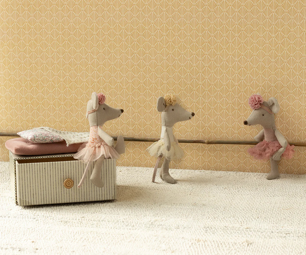 Three stuffed mice, dressed as ballerinas in pink, white, and peach tutus, partake in a ballet class. The Maileg Ballerina Mouse - Little Sister (Off White) joins them beside a small cushioned bench against a backdrop of a patterned beige wall. The ballerina mice seem absorbed in practicing their ballet poses and techniques.