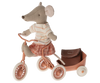 A Maileg Big Sister With Backpack - Coral, dressed in a striped shirt and checkered skirt, rides a pink tricycle with a matching pink wagon attached to the back. The toy mouse, complete with large round ears and a pointed nose, is ready for kindergarten with her tiny backpack.