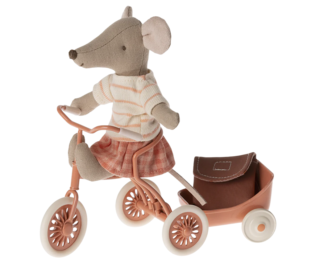 A Maileg Big Sister With Backpack - Coral, dressed in a striped shirt and checkered skirt, rides a pink tricycle with a matching pink wagon attached to the back. The toy mouse, complete with large round ears and a pointed nose, is ready for kindergarten with her tiny backpack.