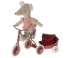 A Maileg Big Sister With Backpack - Red wearing a red-checked shirt and blue shorts sits on a red tricycle, gripping the tricycle handles with confidence. A small red trailer is attached at the back. The toy's fabric has a textured, handmade appearance, perfect for kindergarten playtime adventures.