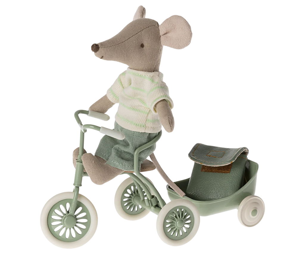 A cute Maileg Big Brother With Backpack - Mint dressed in a green and white striped shirt and green pants rides a small, green tricycle. Attached to the tricycle is a matching green cart carrying a school backpack. The mouse's large ears and tail add to its charming appearance, while hidden magnets in hands provide playful versatility.