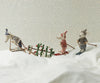 The Maileg Winter Mouse with Ski Set, Big Sister - Rose, features three fabric animal figures skiing in a snowy scene against a polka dot backdrop. One of the mice pulls a tiny sled carrying a decorated tree. Dressed in cozy winter outfits, this charming ski playset creates a whimsical winter scene using recycled polyester for an eco-friendly touch.