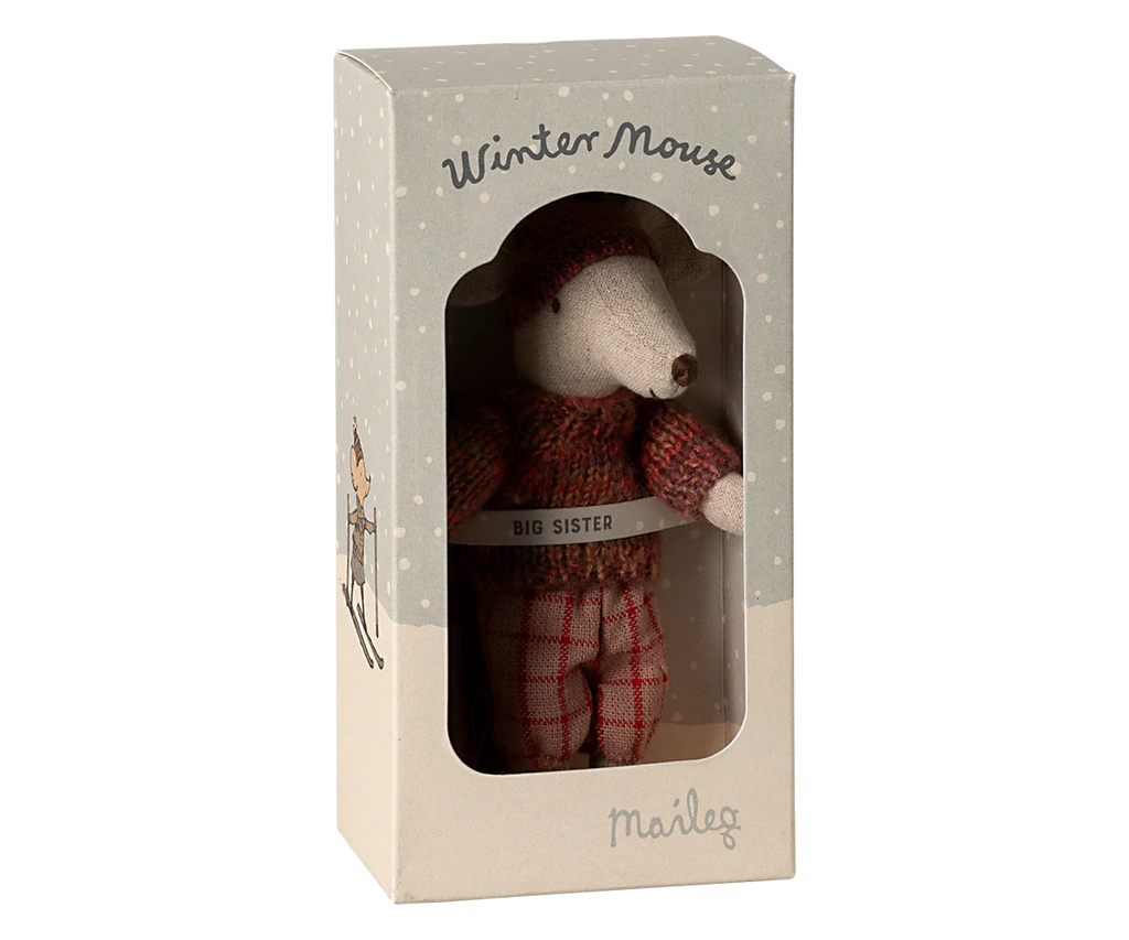 A small winter mouse toy, part of the Maileg Winter Mouse with Ski Set, Big Sister - Rose, dressed in a red knitted sweater and plaid pants, comes enclosed in packaging decorated with snowy designs. The box is labeled "Winter Mouse" and "Big Sister," featuring the brand name "Maileg" at the bottom. It’s crafted from recycled polyester for an eco-friendly touch.