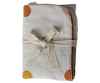 A Maileg Small Blanket - Rose, folded and bound with a natural-colored ribbon, features white linen fabric adorned with orange, yellow, and brown circular patterns, making it perfect for a nursery.