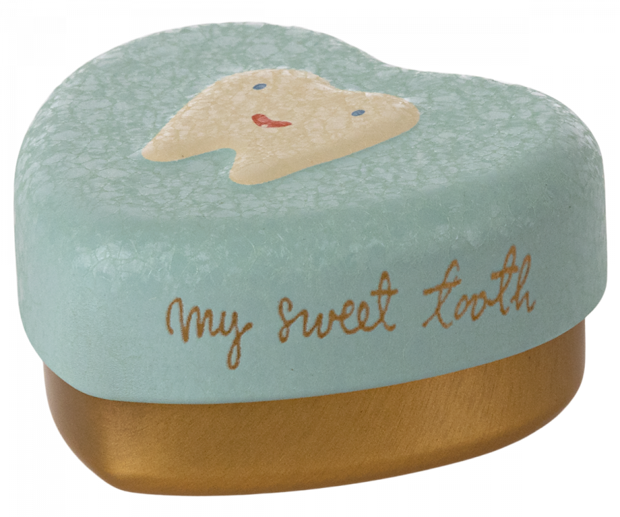 A Maileg Tooth Box with a pastel blue lid featuring a picture of a smiling tooth. The words "my sweet tooth" are written in cursive on the side of the lid. The bottom part of this metal heart keepsake is gold-colored, perfect for preserving precious childhood memories.