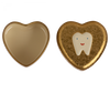 Two heart-shaped objects. The one on the left is a plain, glossy heart. The one on the right is a Maileg Tooth Box, a textured, gold-colored metal heart keepsake with an illustration of a tooth that has a smiley face on it.