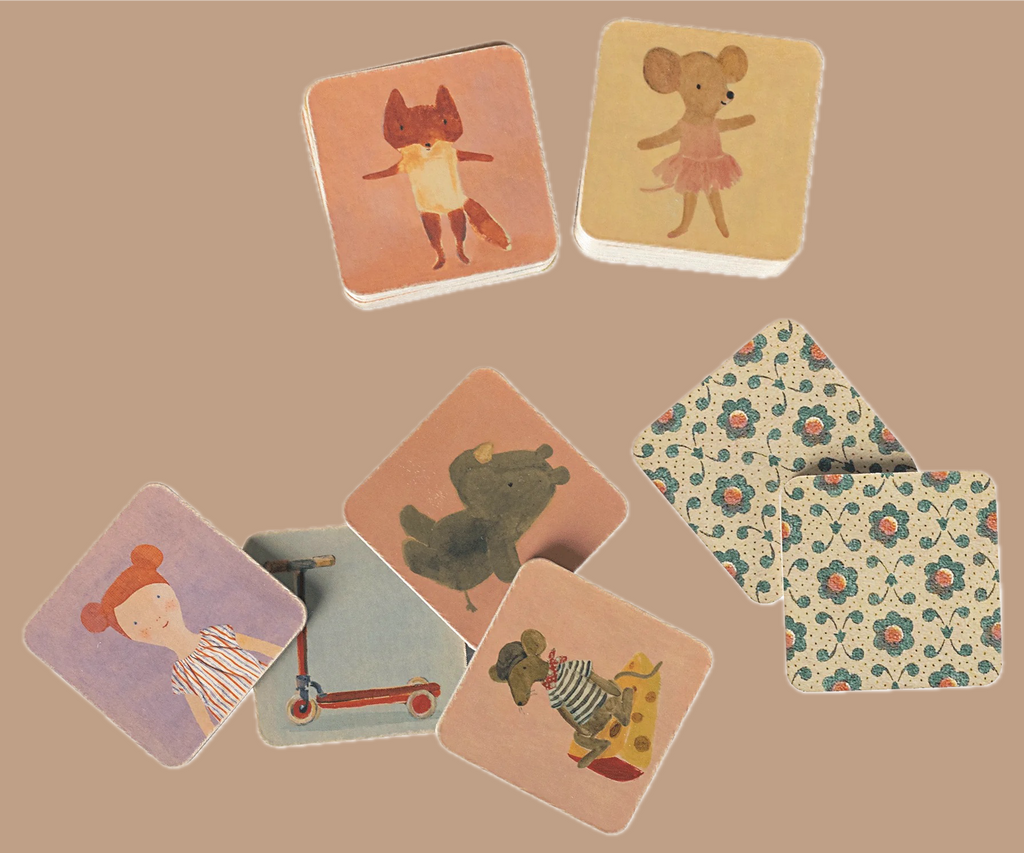 The Maileg Memory Game is a set of illustrated square cards similar to a classic memory game, showcasing animals such as a fox, a mouse in a striped shirt, and a bear. Additionally, some of the cards feature floral patterns. Dorthe Mailil's delightful illustrations bring whimsy to the game, including one that features a scooter.