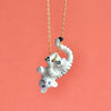 A cute, white tiger cub pendant is attached to a 24k gold plated steel chain necklace. The Gold Tiger Necklace features the cub playfully hanging upside down with its tail curled around the chain. This hand-painted porcelain charm stands out beautifully against the solid coral background.