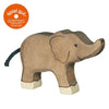 A wooden toy elephant with a smiling face and grey rope tail is shown. The Holztiger Elephant, Small, made in Europe, features handcrafted wood with brown coloring, lighter-colored feet, and ear accents. "Spiel gut," a recommendation label, is placed in the top left corner.