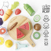 A flat lay image features the Wooden Chopping Board & Sliceable Play Food, including toy fruits and vegetables like watermelon, kiwi, and carrot, set against a light background. The set comes with a toy knife and icons demonstrating the enhancement of fine motor skills through interactive role play.