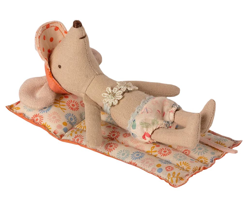 The Maileg Beach Float, Mouse - Flower is lying on a small quilted mat with a colorful flower pattern. The mouse toy features a floral pattern diaper and a flower decoration on its chest, giving it a charming look. The raft-like fabric of the mat makes it perfect for dry land play. With its eyes closed and sporting a content expression, the mouse looks as though it is relaxing or sleeping.