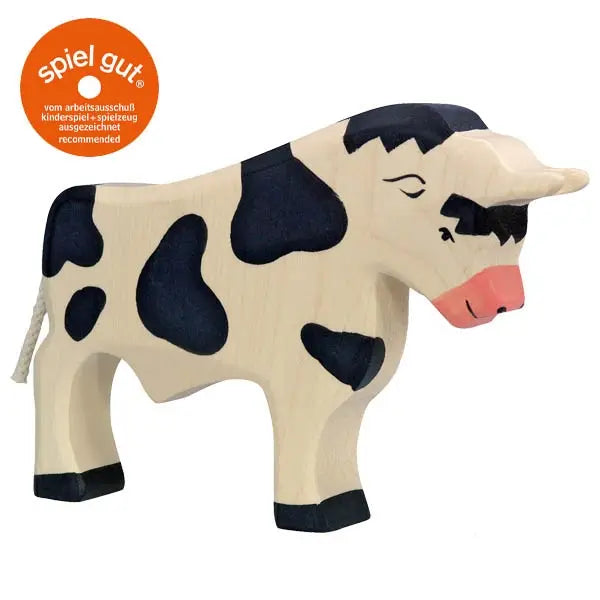 A handcrafted wooden toy cow with a white body and black spots. It features a prominently visible udder and a pink snout. Simply crafted with minimal detail, this charming piece from the Holztiger Bull collection includes an orange "spiel gut" sticker in the top left corner, recommending it for children's play.