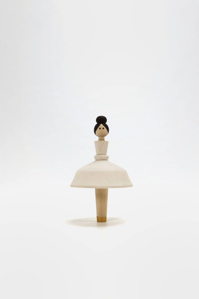 Introducing the Wooden Ballerina: a hand-painted, minimalist wooden spinning top with a Ballerina figure. It features a round base that resembles a skirt and a simple head adorned with a bun hairstyle, positioned elegantly against a plain white background.