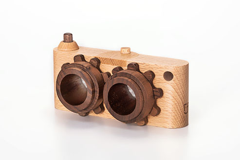 Introducing the Twinkle Kaleidoscopic Camera, a handmade masterpiece with a minimalist design. Crafted from high-quality walnut and beech wood, it features two kaleidoscopic lenses with gear-like edges and a small viewfinder on top. The light-colored body includes a tiny side hole for added charm.