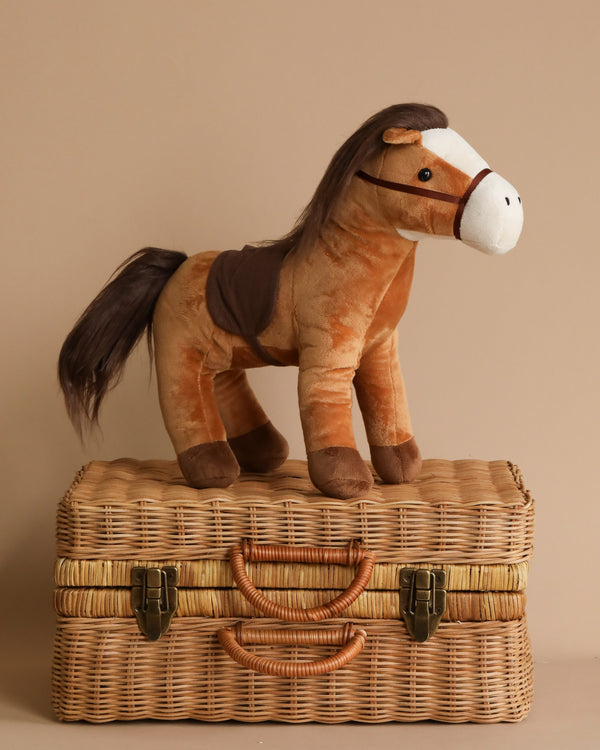 A soft and snuggly Stormy the Horse Stuffed Animal on a wicker suitcase.