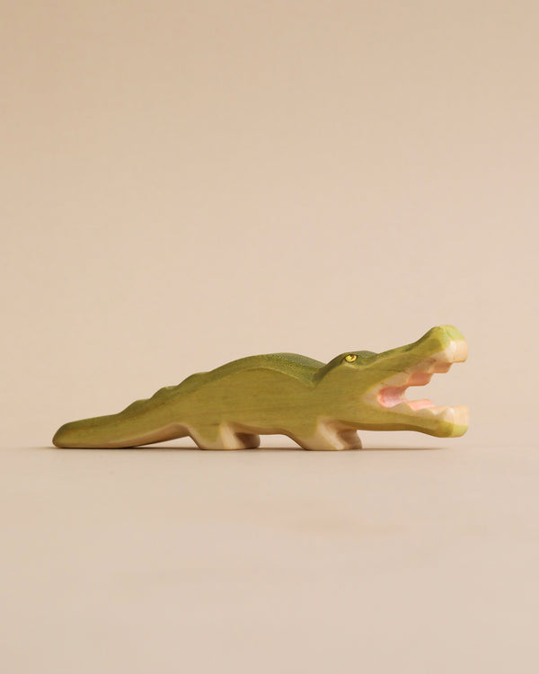 A Handmade Holzwald Crocodile on a plain beige background, standing with its mouth open, showcasing detailed carvings and a smooth green finish.