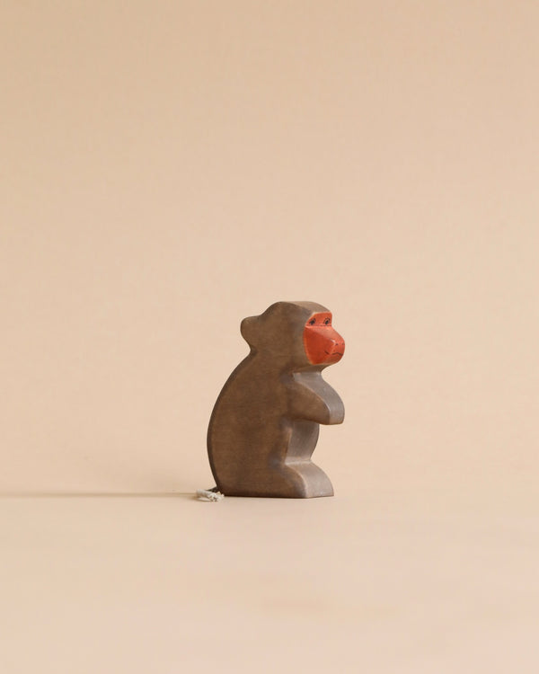 A small, stone monkey statue with a bright red face, sitting in a contemplative pose against a plain, light beige background from Holzwald Brand.
 
Product Name: Handmade Holzwald Baboon