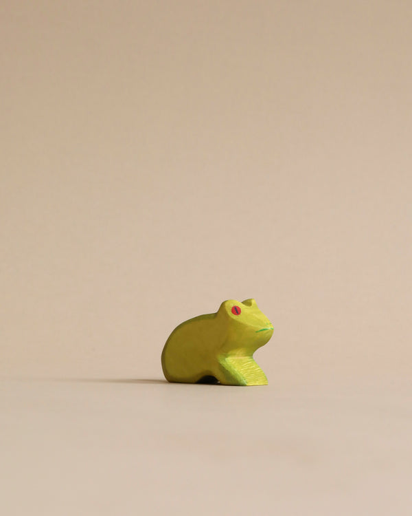 A small, yellow Handmade Holzwald Frog with red eyes, positioned centrally against a plain, light beige background treated with high-quality oil.