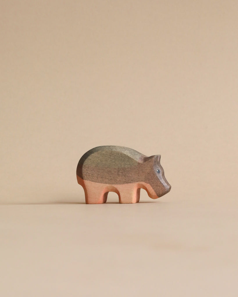 A Handmade Holzwald Small Hippo wooden figurine standing against a beige background, showcasing natural wood grain and a smooth finish.