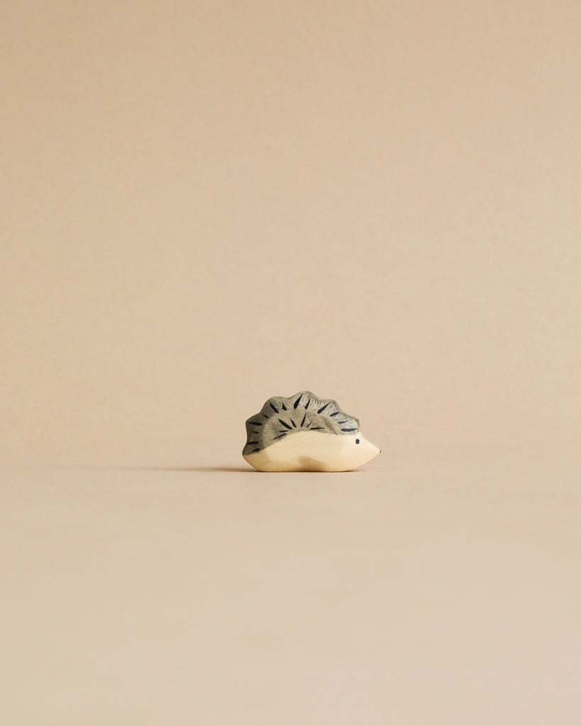 A minimalist image of a small, intricately patterned Handmade Holzwald Hedgehog Baby sculpture with a textured surface, shaped like a star, placed against a light beige background.