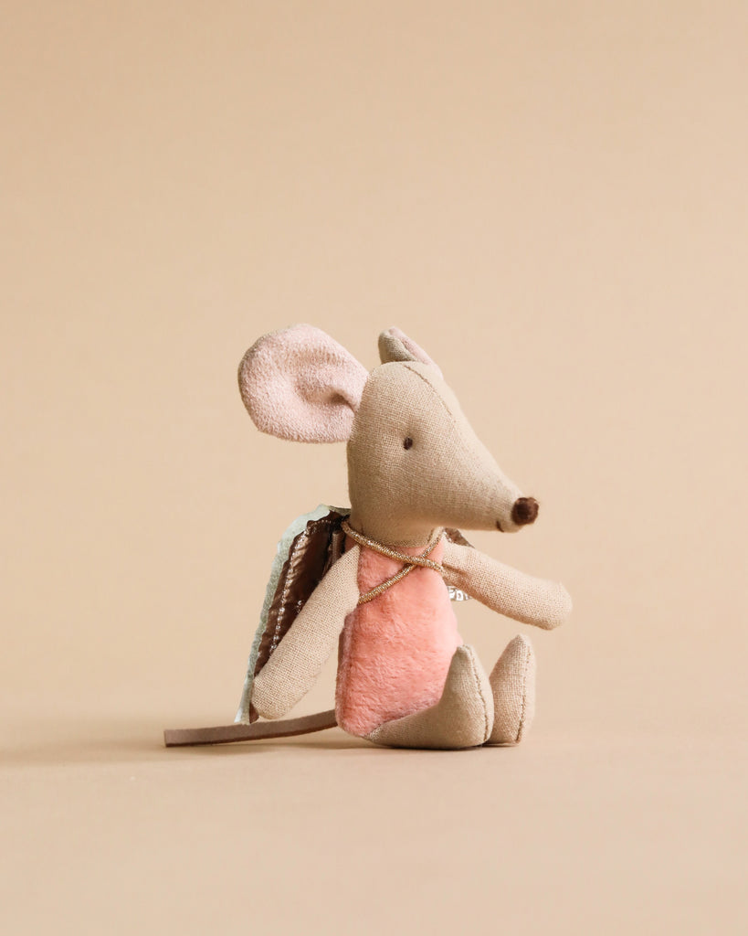 A Maileg Fairy Angel Mouse - Rose with large ears, a long tail, and a pink dress sitting against a neutral beige background. Its arms and legs are flopped to the side, and it has a simple stitched face with a tiny brown nose, evoking wondrous stories of fairy mice in magical moments.