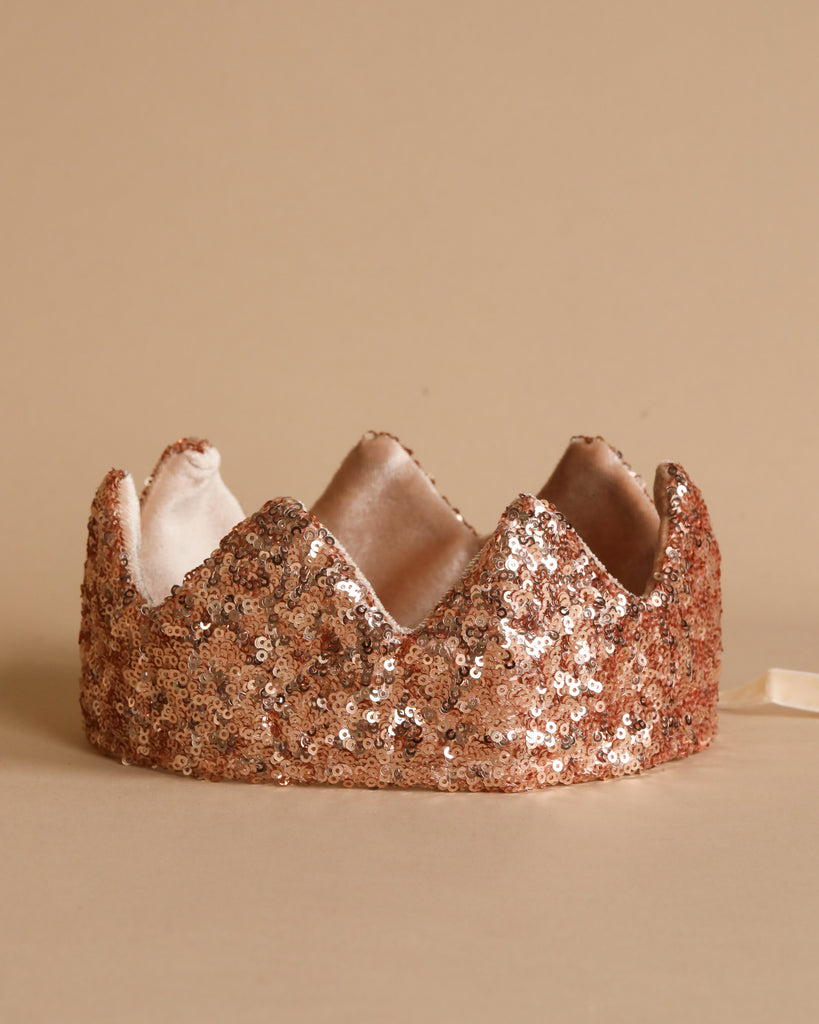 Introducing the Crown - Pink Sequins from Luciole et Petit Pois: a dazzling crown that boasts a pattern of triangular peaks along the top edge. The exterior glistens with sparkling pink sequins, perfect for future Queens. Inside, it features a plush beige fabric lining for ultimate comfort.