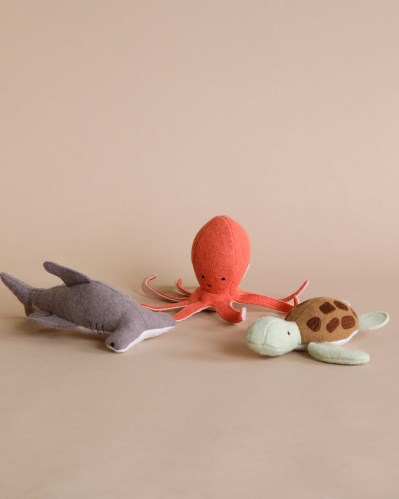 Three Olli Ella Holdie Folk Felt Marine Animals—a gray shark, an orange octopus, and a green and beige turtle—displayed against a pale background.