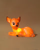 The Resin Deer Lamp, a glowing, deer-shaped children's night light with a cute and cartoon-like design, sits on a plain background. This LED light features large, expressive eyes, big ears, and a peaceful expression while casting a warm, orange glow. Perfect for nursery decor, its power cord is visible extending from the lamp.