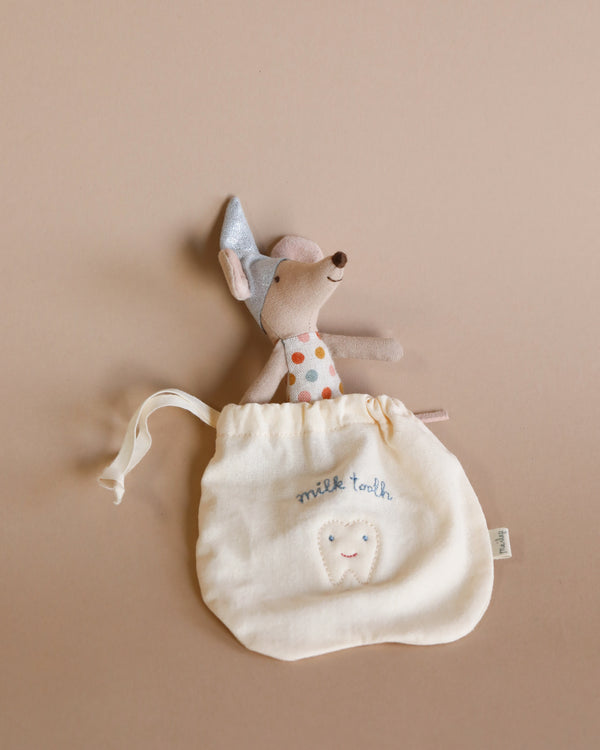 A small fabric pouch labeled "milk tooth" with a tooth illustration, accompanied by a Maileg Tooth Fairy Little Mouse wearing a polka-dotted shirt and a pointy hat, partially sticking out of the cute little bag on a beige background. Perfect for keeping those precious baby teeth safe until the tooth fairy arrives.