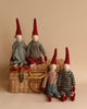 Four Maileg Christmas Pixies (Size 3) with tall red hats and simple facial features sit on and around a wicker basket. Resembling festive pixies in their knitted and striped outfits, they add a cozy, handmade charm to the scene. The background is a plain, warm beige. Perfect as Christmas decorations!