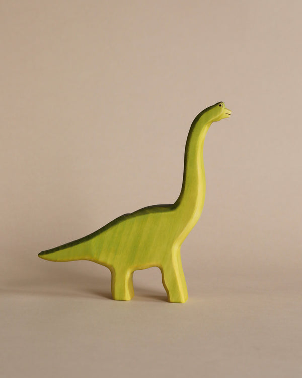 A sustainable Handmade Holzwald Brachiosaurus - Green, specifically a brachiosaurus, stands against a plain, light beige background.