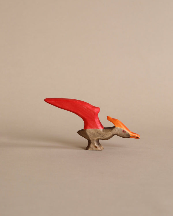 A small sustainable Handmade Holzwald Pteranodon with a bright red crest and beak, positioned upright against a plain, light beige background.