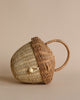 A handwoven Olli Ella Rattan Acorn Bag shaped like a fish, featuring intricate details and a small clasp, set against a soft beige background.