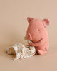 A pink plush toy resembling a piglet with polka-dotted inner ears sits against a soft beige background. Next to it is a white polka-dotted cloth with a knot, lying on the ground in front of the toy—a perfect baby gift from the Maileg Lullaby Friends - Pig (Plays Music) collection.