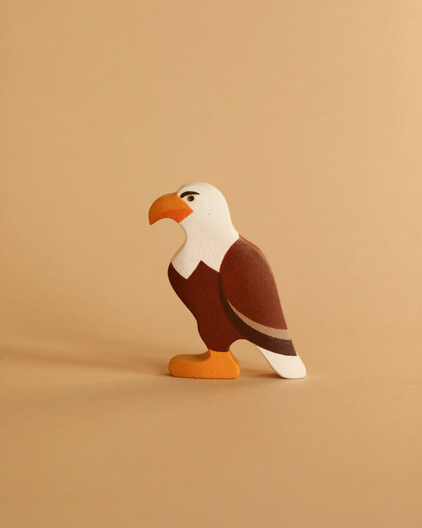 A Handmade Wooden Eagle with a white head, brown body, and orange beak is displayed on a beige background. This charming product is ideal for small world play, featuring a meticulous hand-painted finish that enhances its delightful appeal.