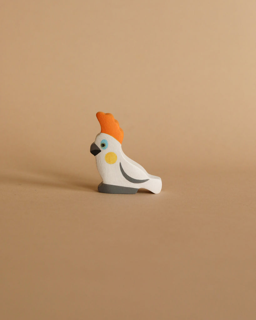 A Handmade Wooden Cockatoo, featuring a white body, orange crest, and black beak, rests on a simple beige background—ideal for small world play.