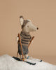 The Maileg Winter Mouse with Ski Set, Big Brother in Grey stands on a bed of fake snow, capturing the essence of winter excitement in its cozy knitted sweater and hat. Clutching brown ski poles and with skis securely fastened, it's poised for a whimsical skiing escapade against a simple beige background.