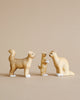 The Handmade Wooden Cat Family features three handcrafted wooden cat figurines displayed against a beige background. One cat stands on all four legs with its tail curled upward, another cat is sitting on its hind legs, and the third sits upright. Made from Romanian ash wood and finished with water-based paint, they boast white paws and a light brown color.